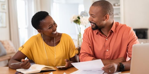 Cheerful mature couple sitting and managing expenses at home. Happy african man and woman paying bills together and managing budget. Black smiling couple checking accountancy and bills while looking at each other.